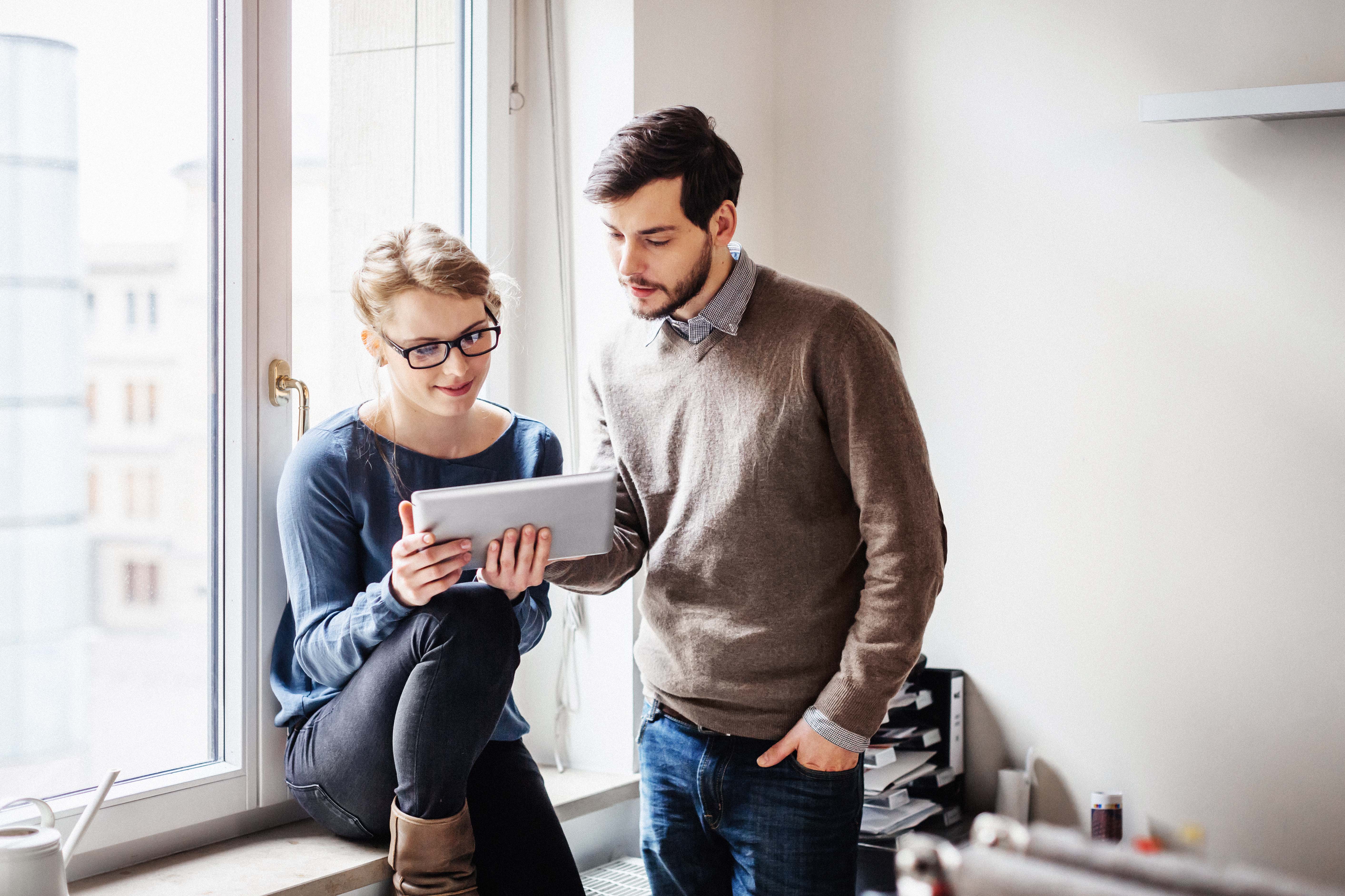 Two people in conversation while one person is showing something on a tablet to the other