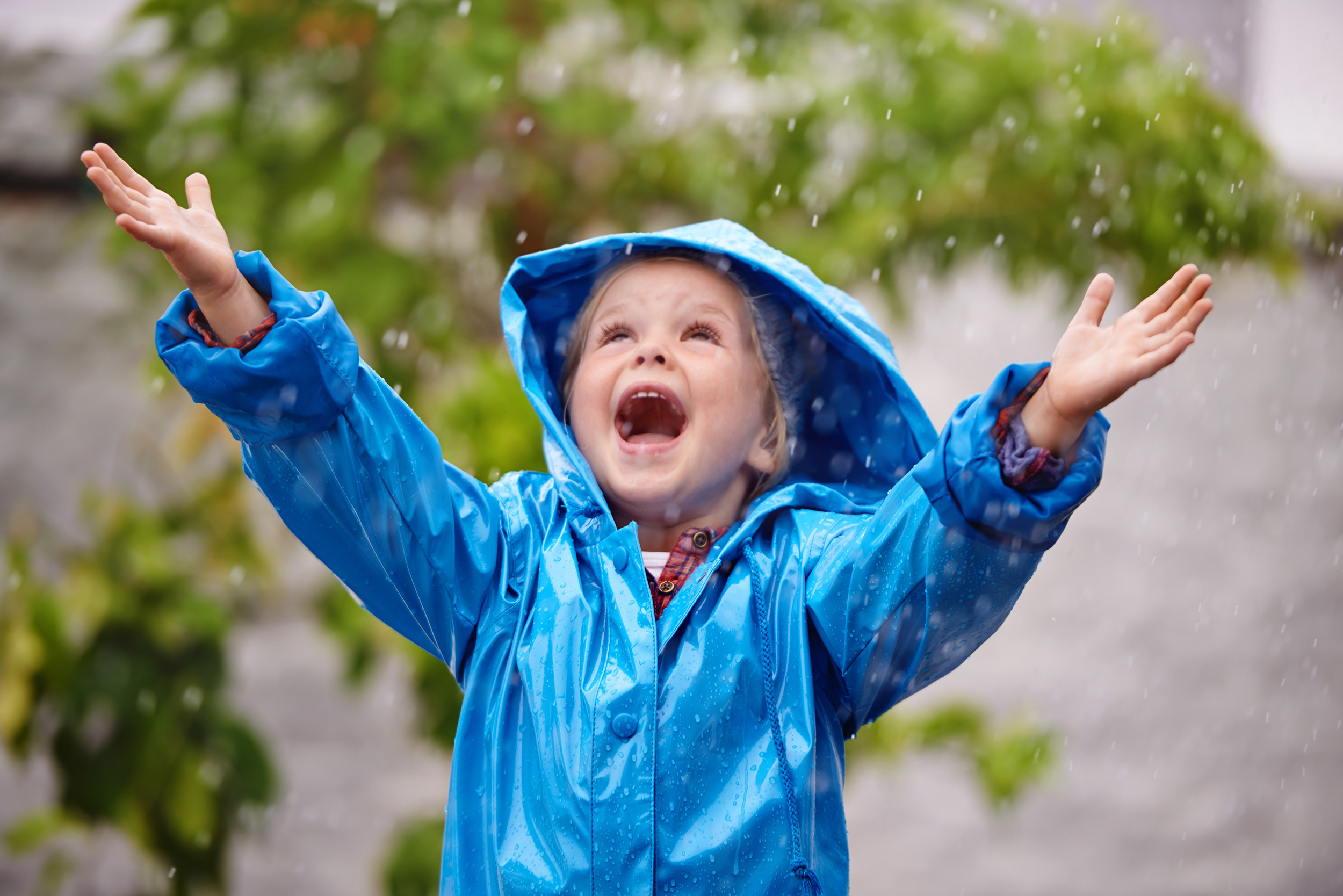 Child with blue raincoat standing in the rain