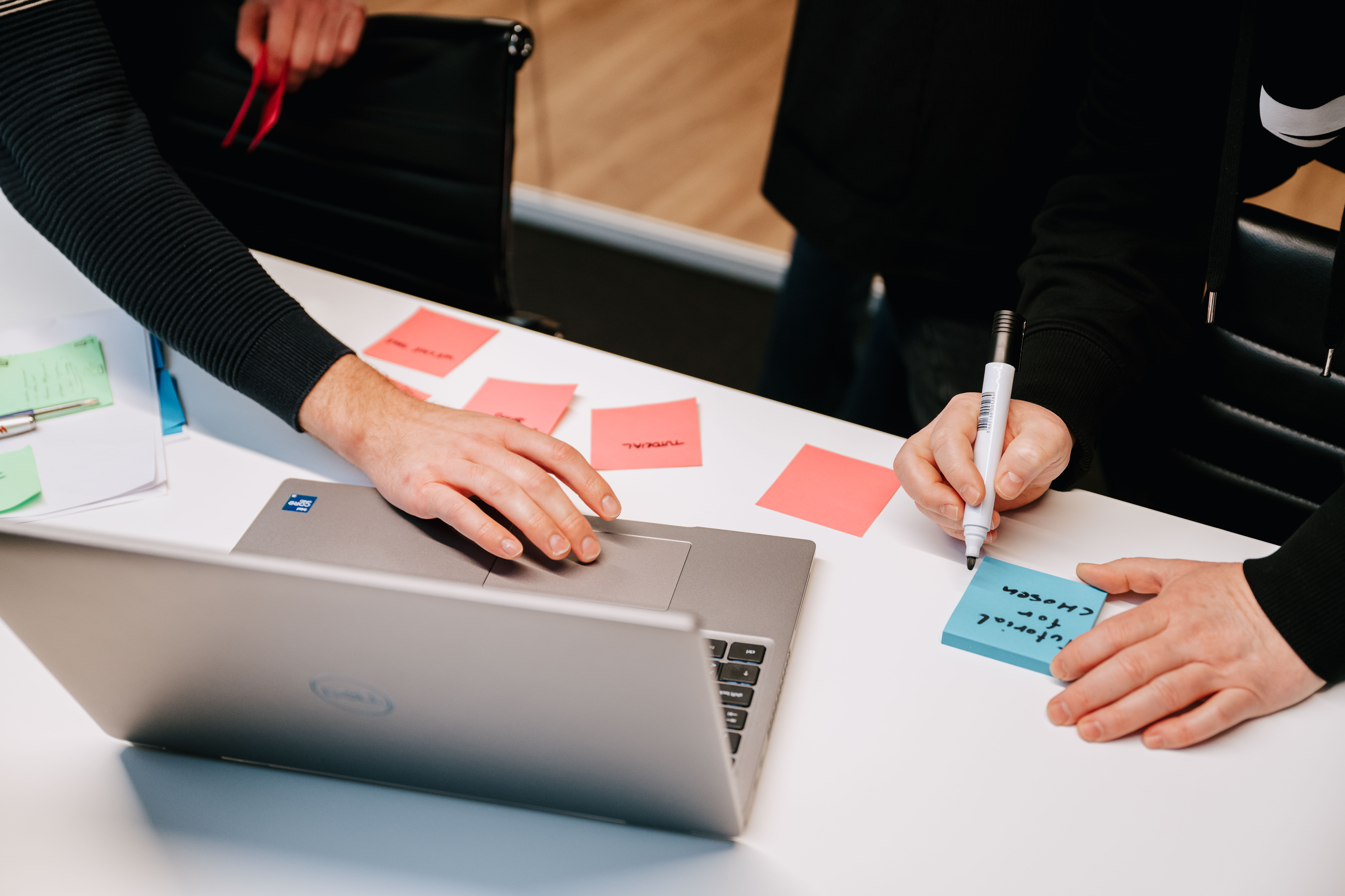 Top view of a laptop with people writing on sticky notes around it