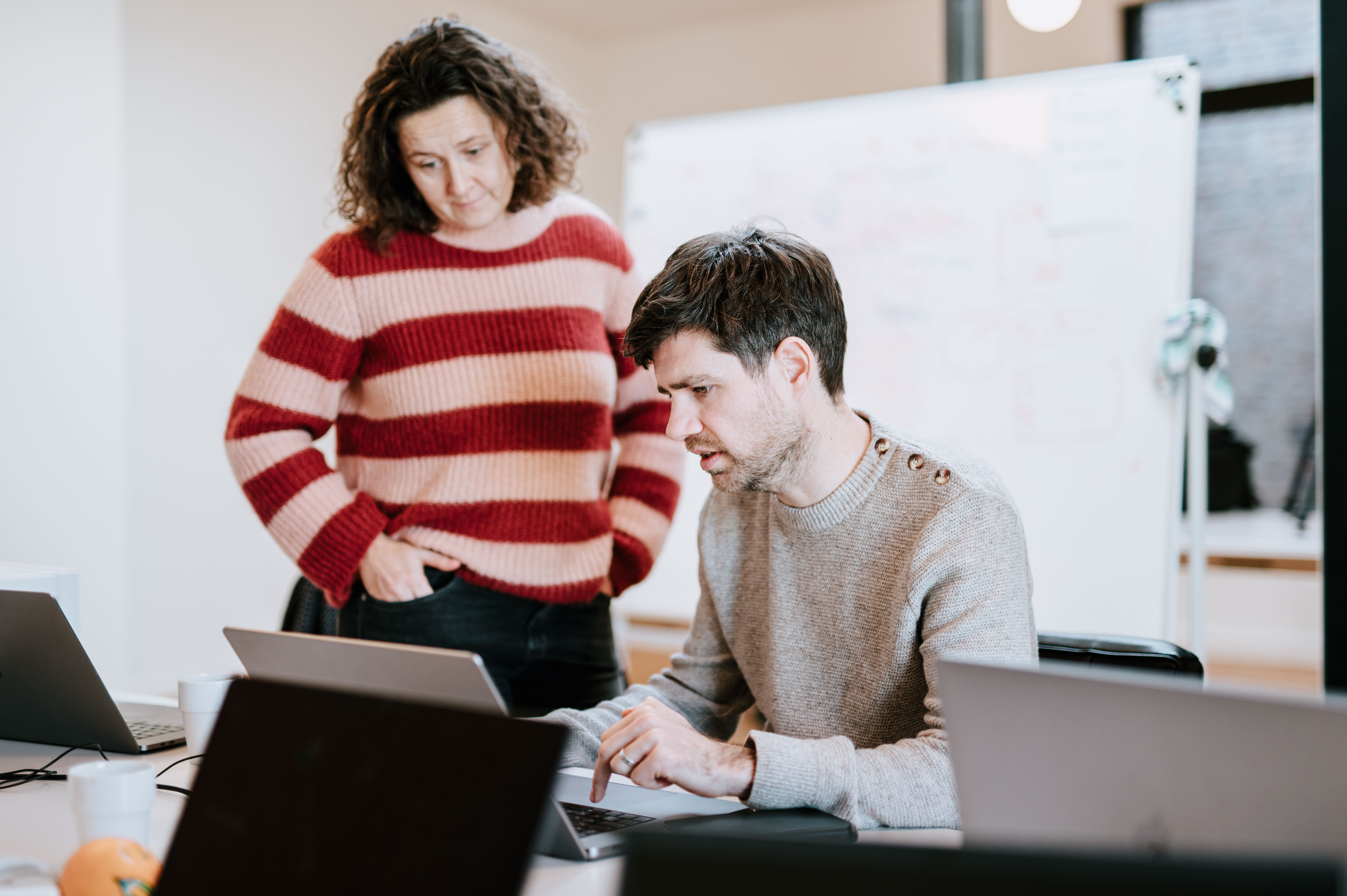 Two colleagues staring at a laptop screen with one sitting on a chair while the other one is standing straight