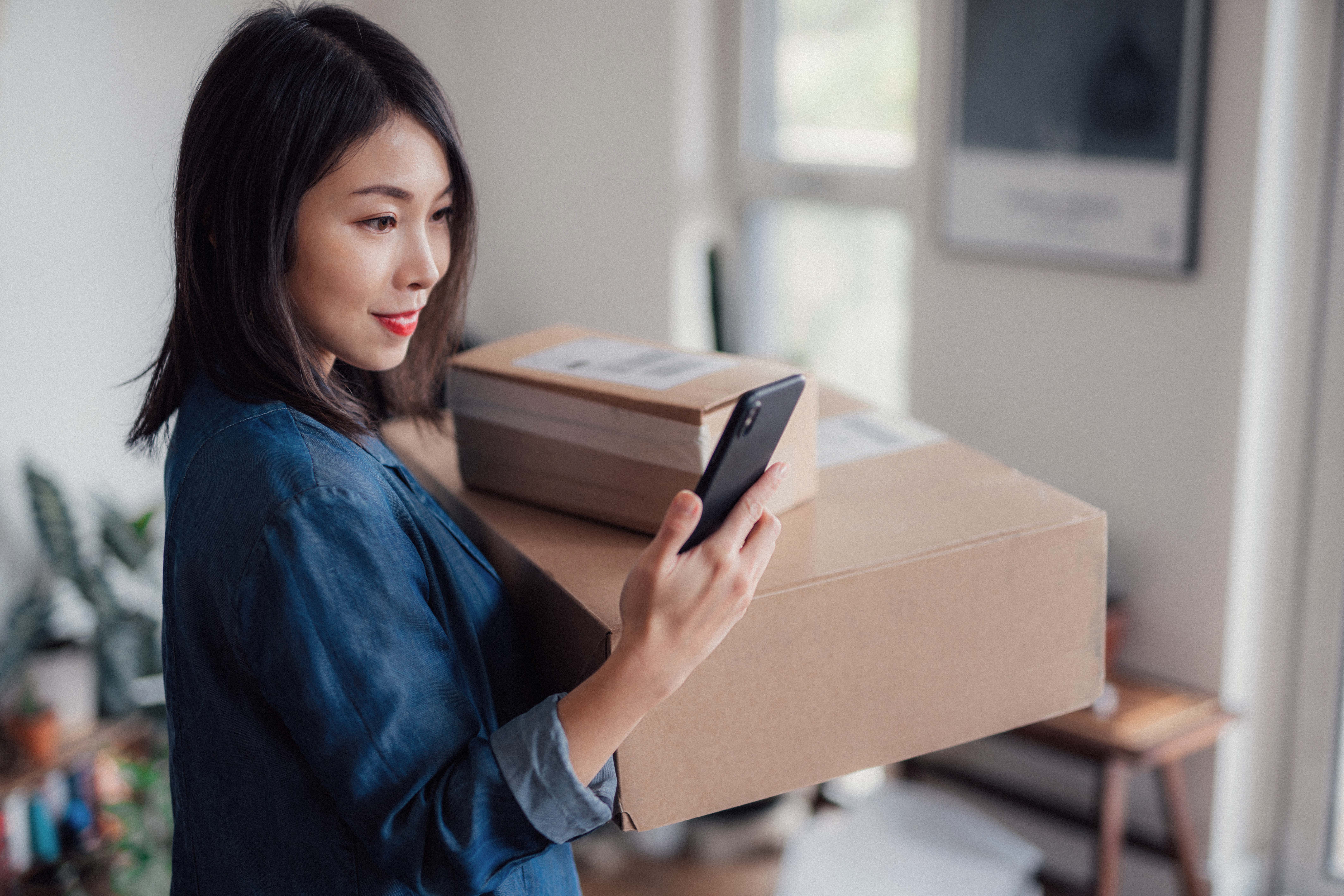 Person checking phone while carrying cardboard boxes