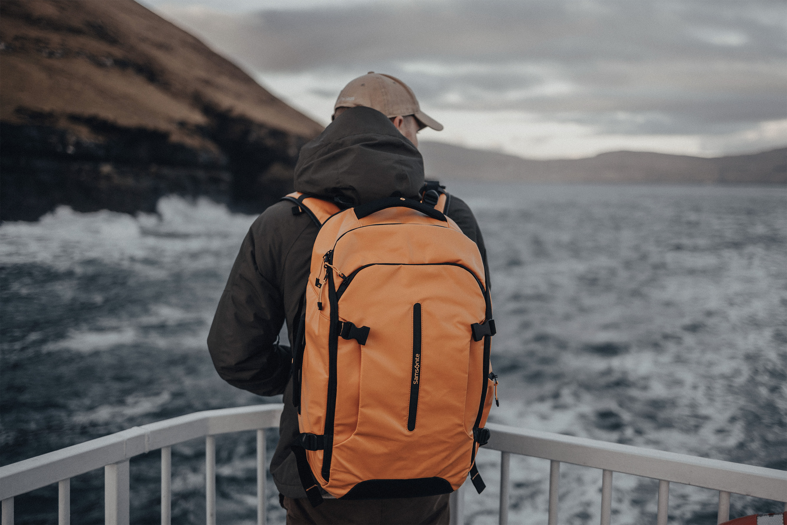 Person standing on a balcony near water with a Samsonite backpack