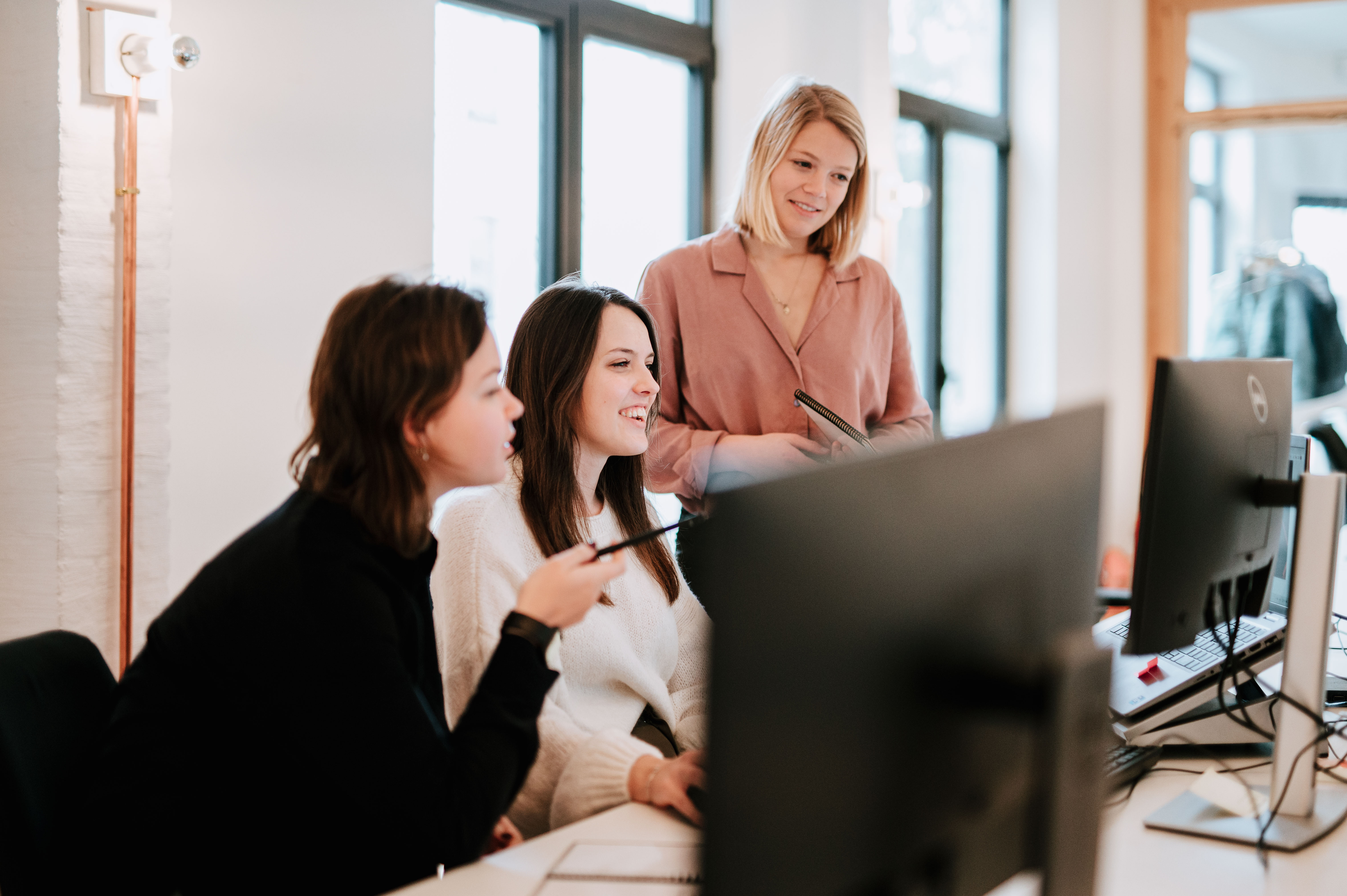 Three people looking at a computer screen, pointing at something on the screen