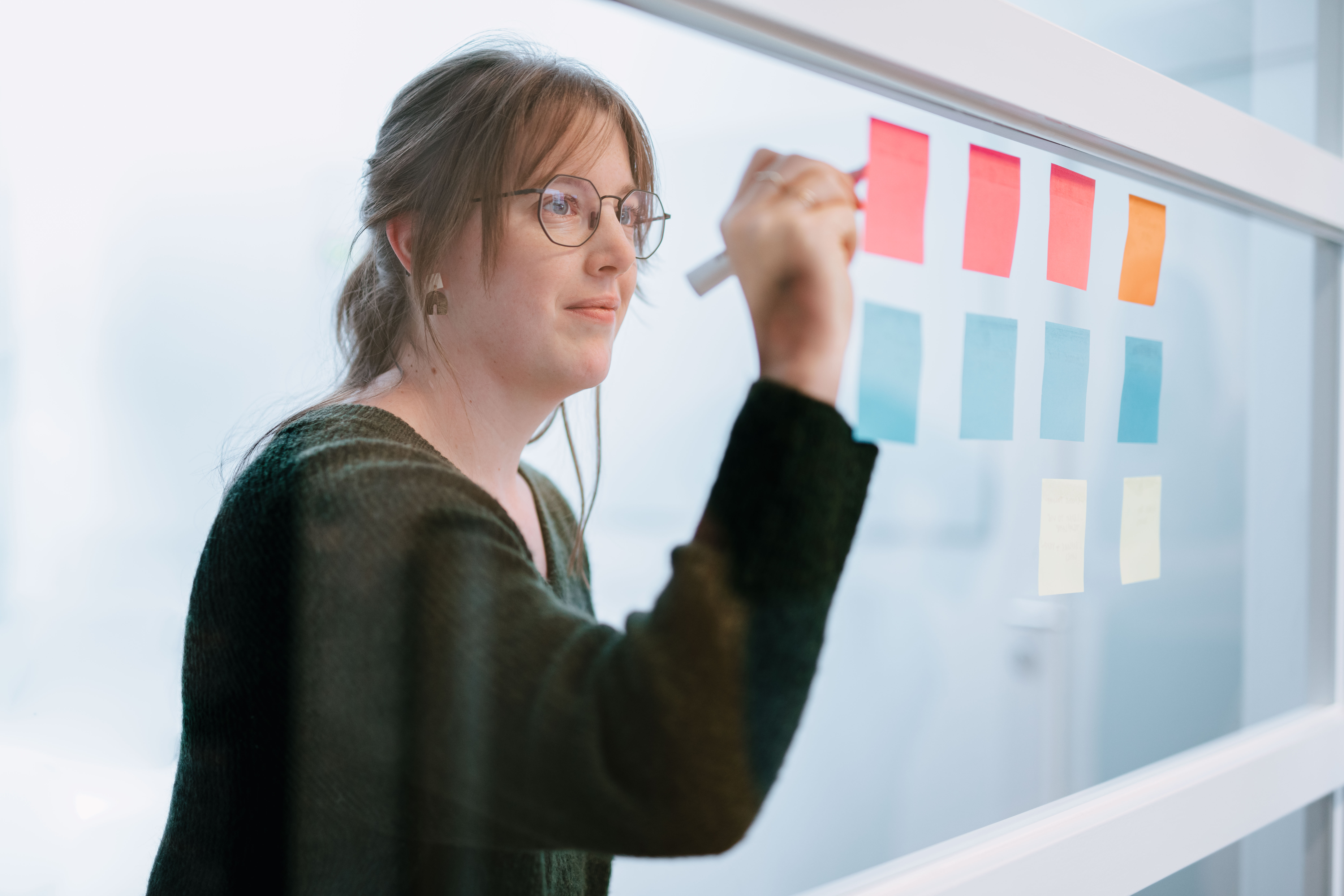 Person writing on a post-it hanging on a glass wall 