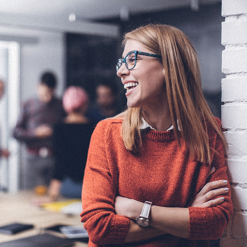 Person smiling at work leaning against a wall 